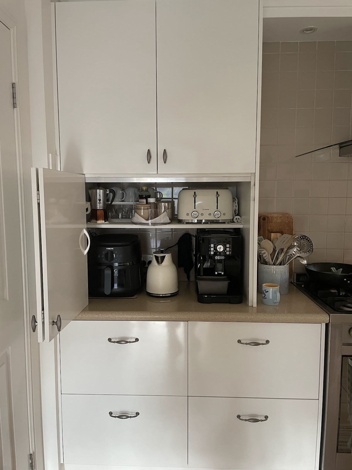 An appliance cupboard with the door open, showing an air fryer, kettle, coffee machine and toaster