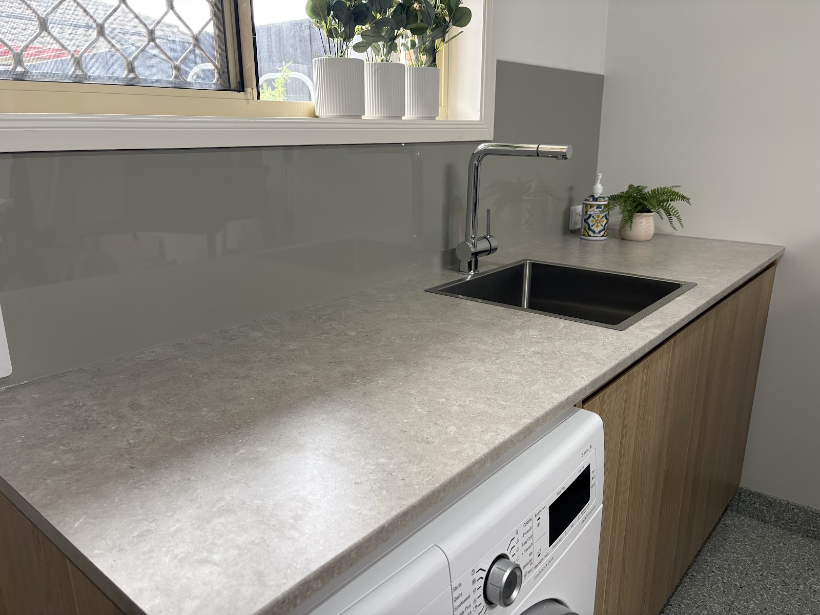 The same laundry after: stone-look benchtop, inset sink, glass splashback and timber-look cabinets
